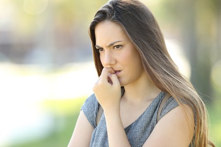 nervous woman biting nails and looking away alone outdoors in the street
