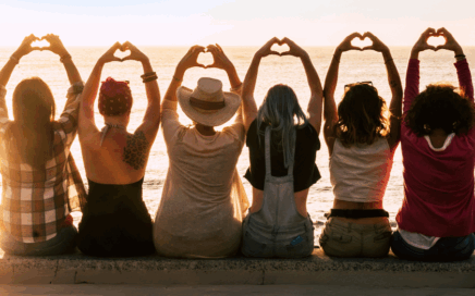 Group of girlfriends together on a wall making heart shapes with their hands