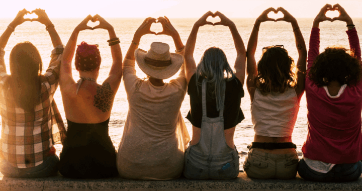 Group of girlfriends together on a wall making heart shapes with their hands
