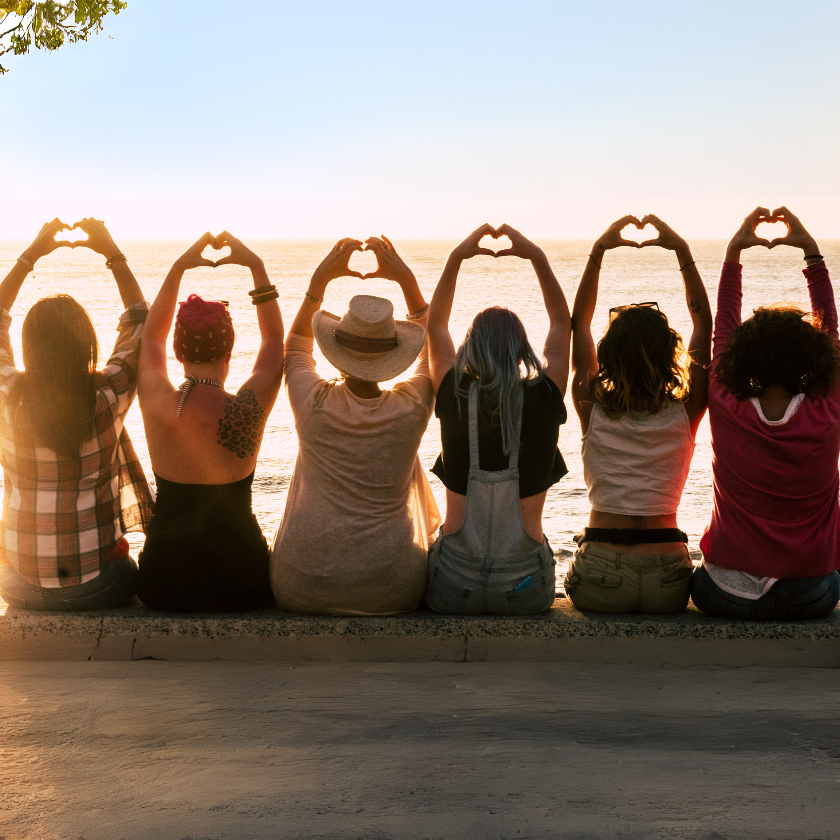 Group of girlfriends together on a wall making heart shapes with their hands